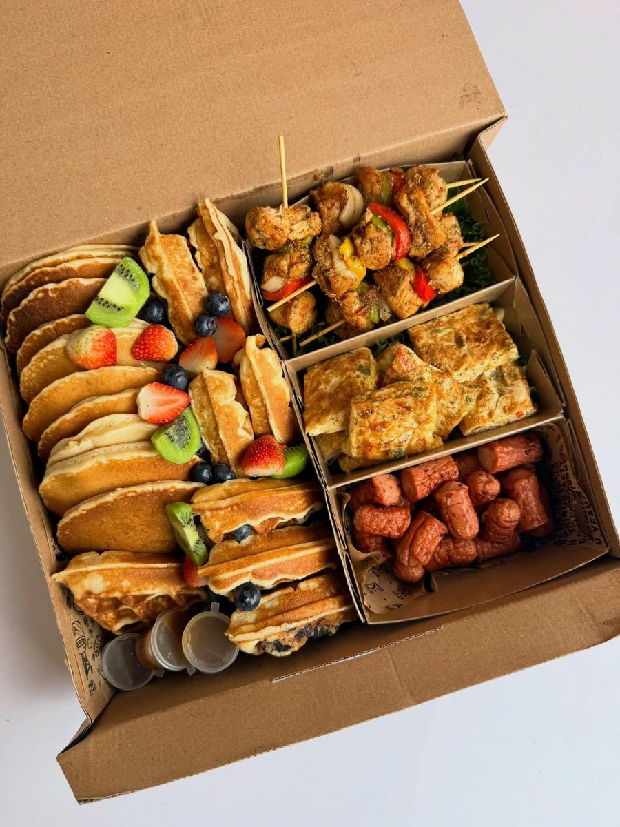 Kraft catering box with compartments filled with pancakes, waffles, chicken skewers, omelette and sausages