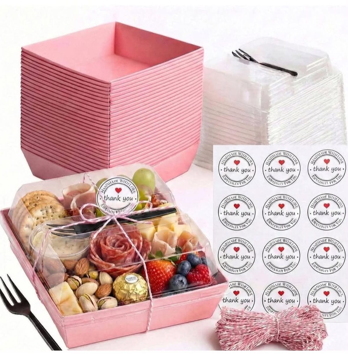 Pink square box with clear lid holding a charcuterie and fruit selection, with thank-you stickers and twine