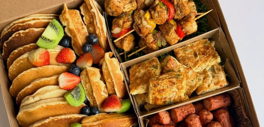 Kraft catering box with compartments filled with pancakes, waffles, chicken skewers, omelette and sausages